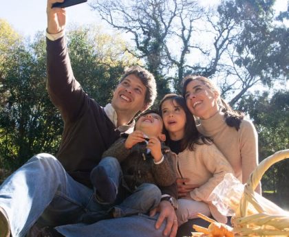 Happy family taking a selfie during a sunny picnic in a park.